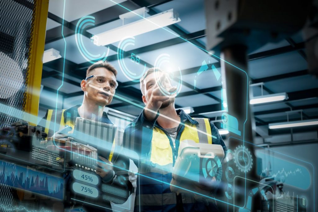 Two industrial workers reviewing digital performance data on a transparent screen in a production setting.