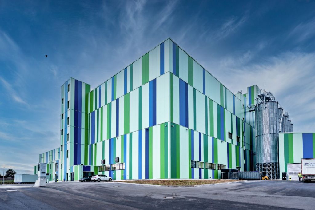 Exterior of BENEO’s pulse-processing plant in Offstein, Germany, with striped green and blue facade and grain silos.